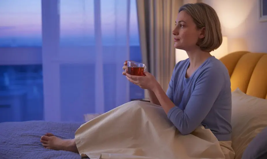 Woman sitting on bed at twilight holding herbal tea, representing sleep quality concerns on Mounjaro treatment