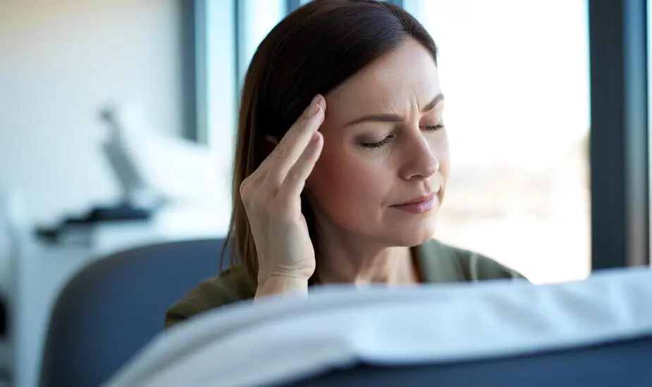 Woman sitting in a calm clinical consultation room, touching her temple, illustrating dizziness on Mounjaro